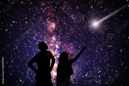 Silhouettes of father and daughter under starry skies.