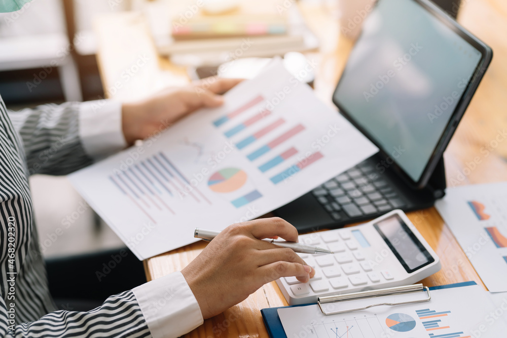 Close-up of businesswoman using calculator with analyzing chart and graph showing changes on the market. Close-up of businesswoman using calculator with analyzing chart and graph showing changes on the market.