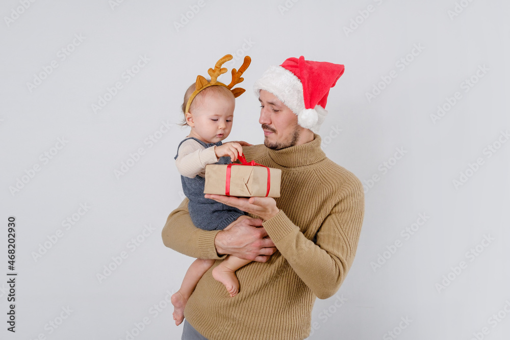 Obraz premium A funny baby being hold by father wearing Santa Claus hat unpacks a Christmas box