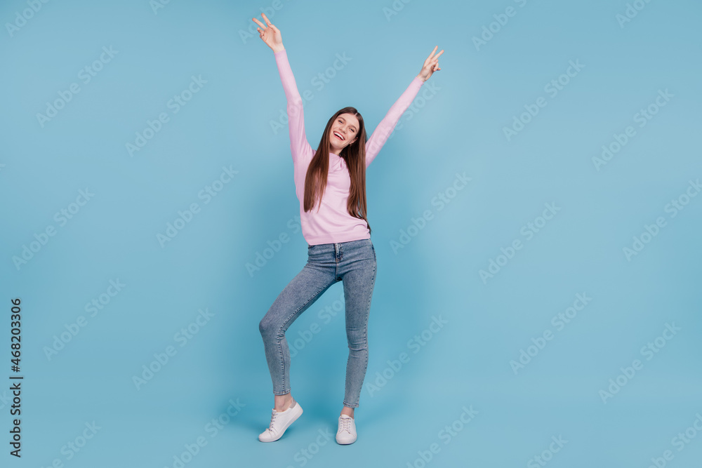 Full size photo of young cheerful girl happy positive smile show peace cool v-sign isolated over blue color background Full size photo of young cheerful girl happy positive smile show peace cool v-sign isolated over blue color background