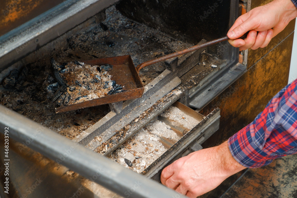 Ash removal from the fireplace. A man's hand in a plaid shirt holds a