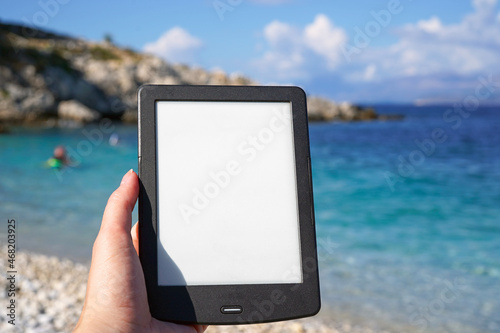 Fototapeta Naklejka Na Ścianę i Meble -  hand holding e-book reader on the beach, reading during summer vacation