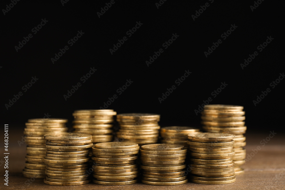 Many coins stacked on wooden table against black background, space for text Many coins stacked on wooden table against black background, space for text