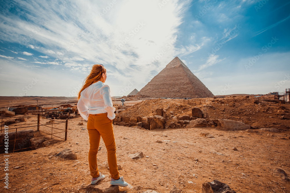 A girl in orange pants - a tourist stands with her back to the camera and looks at the pyramids. Meditation near the pyramids in Cairo, Egypt - obrazy, fototapety, plakaty 