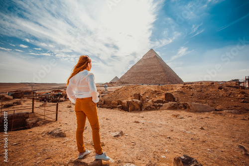 A girl in orange pants - a tourist stands with her back to the camera and looks at the pyramids. Meditation near the pyramids in Cairo, Egypt