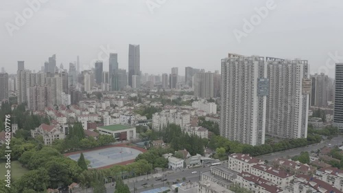 Drone flying over a populous district in Shanghai, China. Big tall residential buildings visible, City business zone with skyscrapers in background. Basketball courts visible.