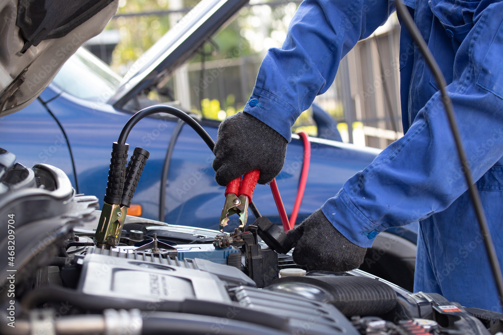 Close up of hand mechanic car service battery with electricity through jumper cables. Service work by professional technicians concept.