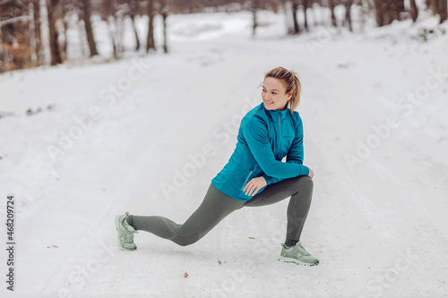Sportswoman crouching in nature on snow at winter and doing warm up exercises. Nature, forest, winter fitness, healthy lifestyle