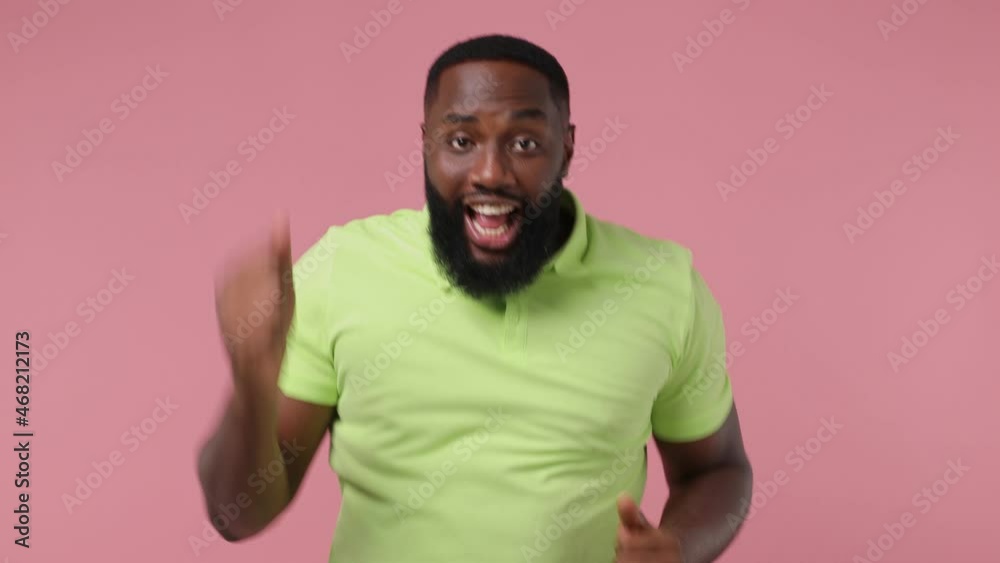 Young african american man 20s wears green t-shirt dance clench fists waving rising expressive gesticulating hands have fun celebrate isolated on plain pastel light pink background studio portrait Young african american man 20s wears green t-shirt dance clench fists waving rising expressive gesticulating hands have fun celebrate isolated on plain pastel light pink background studio portrait