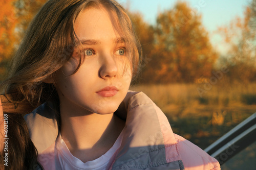 The teenage girl looks thoughtfully to the side. The rays of the sunset illuminate the face of the teenager. Calm, emotionless and aspirational expression photo