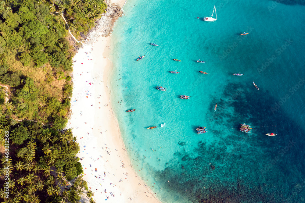 View from above, stunning aerial view of a white sand beach bathed by a turquoise, clear water. Tropical beach with some long tail boats and relaxed tourists. Freedom beach, Phuket, Thailand. - obrazy, fototapety, plakaty 