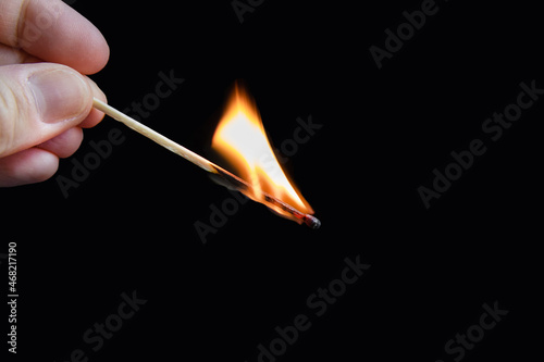 Human fingers holding burning match on black background.