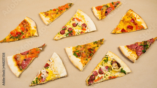 Grop of triangular slices of different types of pizza on a beige kraft paper background.