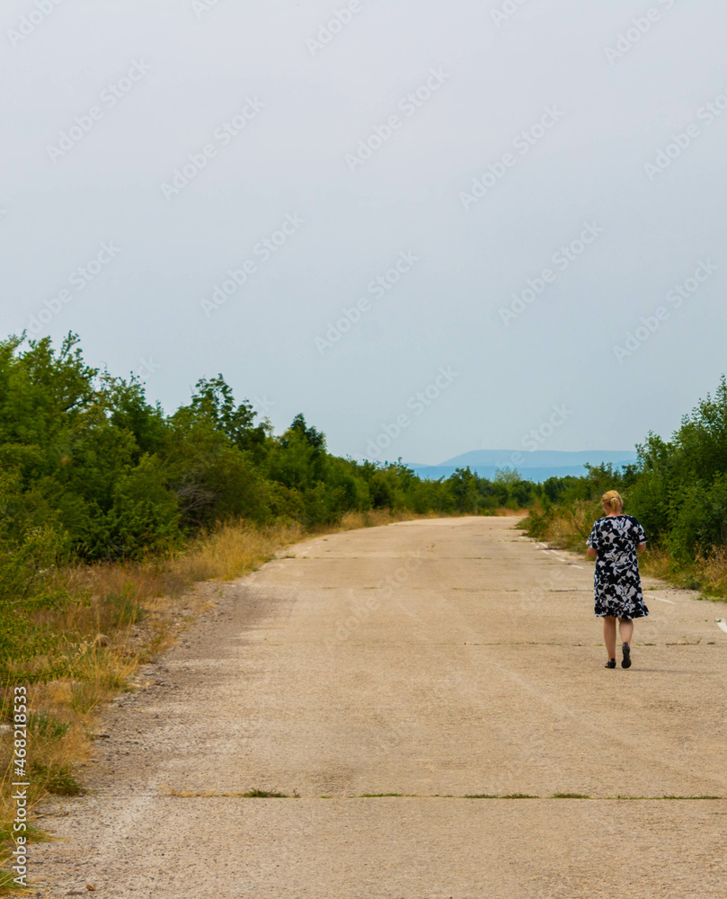 An old asphalt road and a woman walking in the distance; where this woman is going?