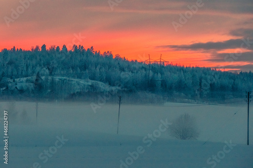 Winter time sunset in rural scene. Beautiful red sky and some fog on a snowy field.