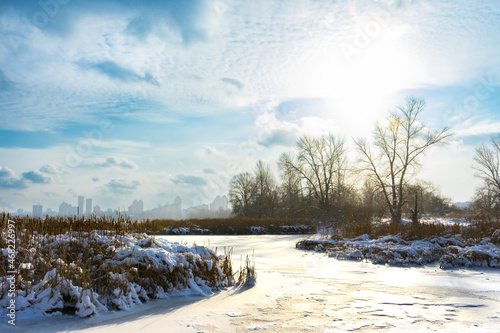 Winter landscape with ice-covered river on snowy cold day with shining sun and blue sky