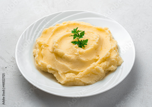Mashed potatoes with basil in a white plate close-up on a gray background.