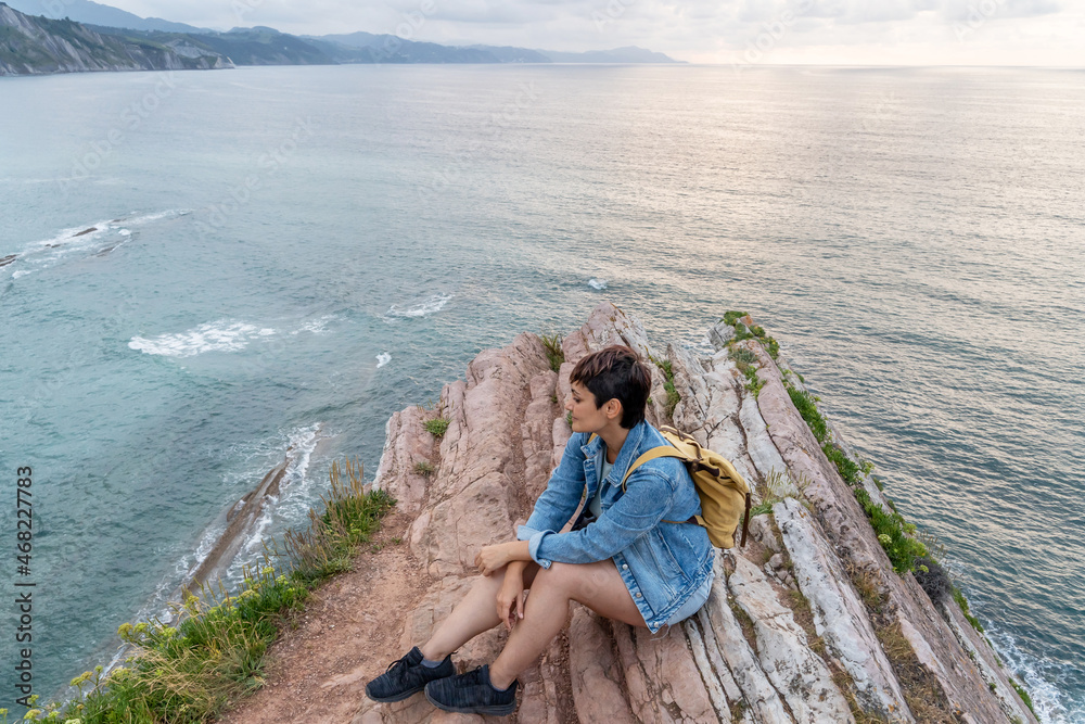 Horizontal view of adventurous traveler woman sightseeing in Zumaia cliffs. Horizontal panoramic view of woman traveling in vasque country. People and travel destination in Spain