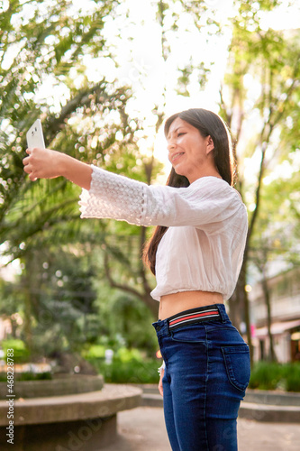young latin tourist woman taking a selfie at sunset in a park, with the sun's rays illuminating her, copy space