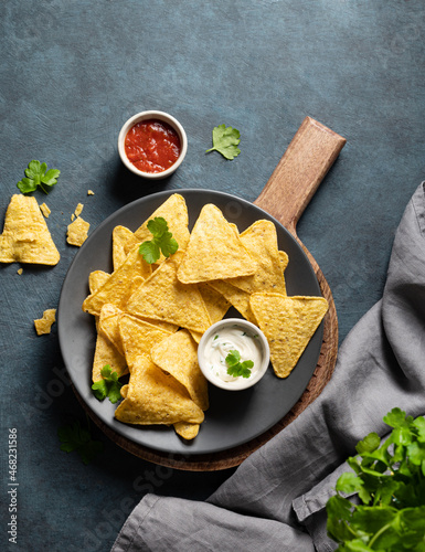 Tradition Mexican food. Corn chips nachos with salsa and cheese sauce and fresh herb on gray plate on dark background. top view and copy space
