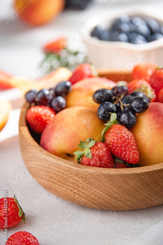 Fresh organic summer berries and fruits of strawberries  blueberries  peaches and grapes in a  wooden plate on a white background. Macro and close up