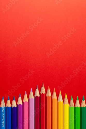 Creative vertical background made of colour pencils on red paper. Flat lay. Education concept.