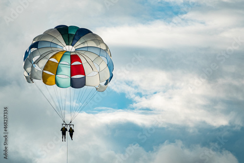 Man and woman are gliding on a colorful parachute on the background of wonderful blue sky