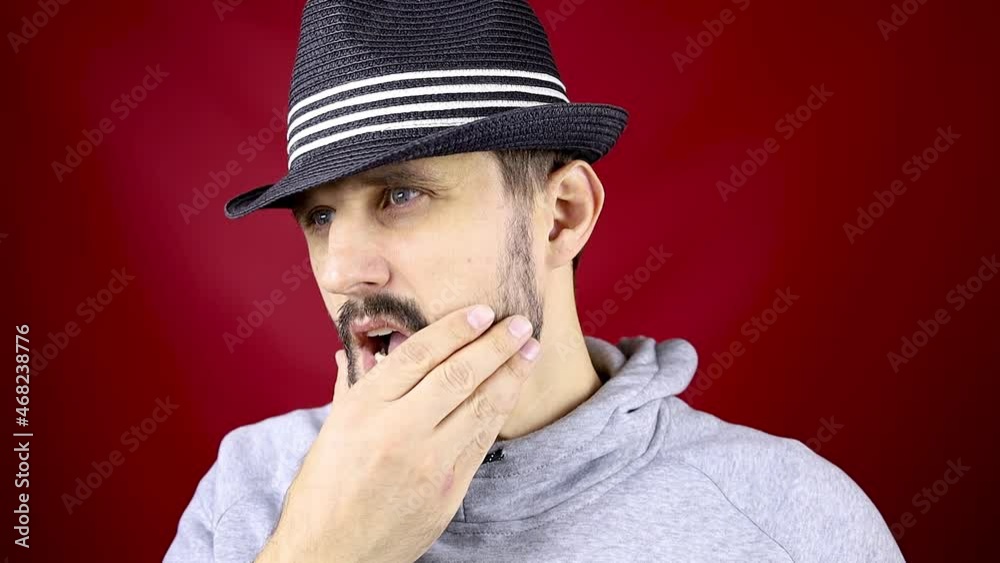 bearded man in a black hat on a red background smoothing his beard with his hand bearded man in a black hat on a red background smoothing his beard with his hand