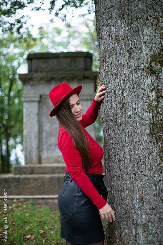 White woman with long dark hair in bright red near the tree trunk