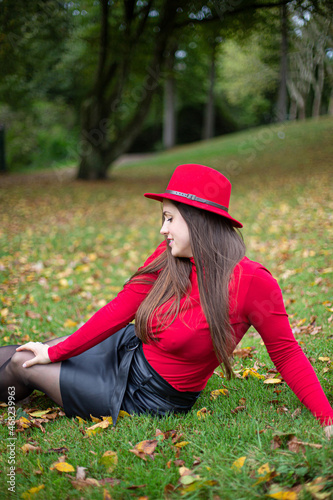 Looking away white woman with long dark hair in bright red in fall park sitting on the grass
