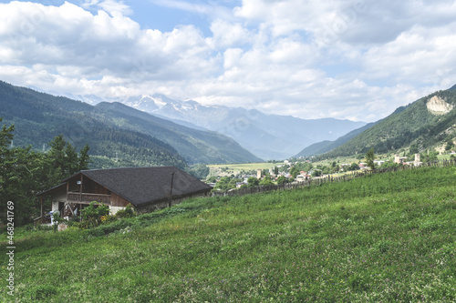 View of highland townlet Mestia in Svaneti region  Georgia. Green meadows  valles and rural houses. Caucasus mountain range  snow capped mountains in the background