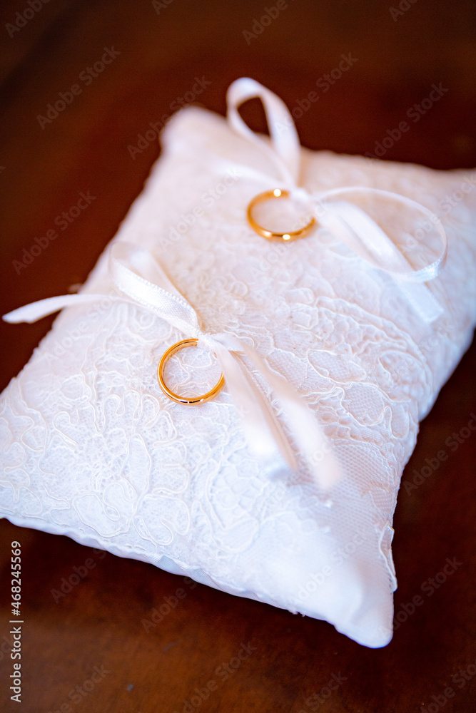 Vertical image of two golden wedding ring lay on white decorative cushion for bride and groom on weddings