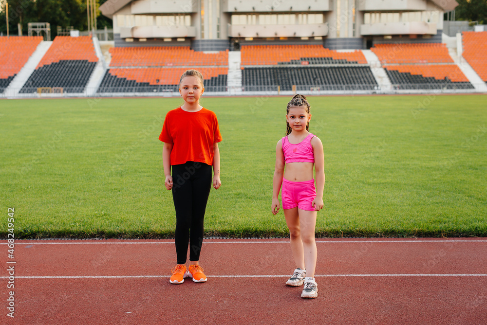 The girls are engaged in warm-up exercises and exercises in gymnastics and acrobatics in the summer at the stadium during sunset. Healthy lifestyle, sports training.