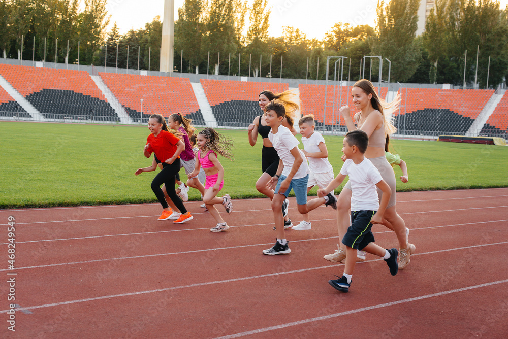 Fototapeta premium A large group of children, boys and girls, run and play sports at the stadium during sunset. A healthy lifestyle.