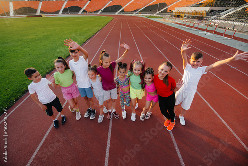 A large group of children, boys and girls, rejoice together and wave their hands at the stadium during the sunset post game. A healthy lifestyle. © Andrii
