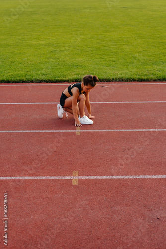 A little girl sat down to tie her shoelaces before running training at the stadium during sunset. Children's sports, and a healthy lifestyle.