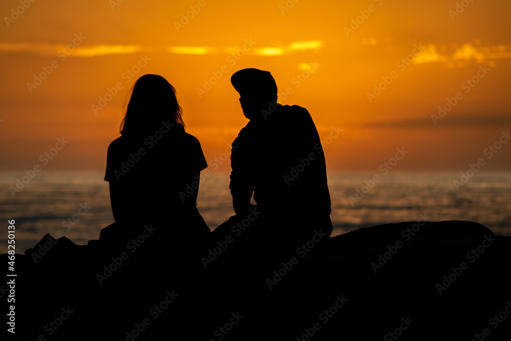 silhouette of a couple on the beach watching sunset