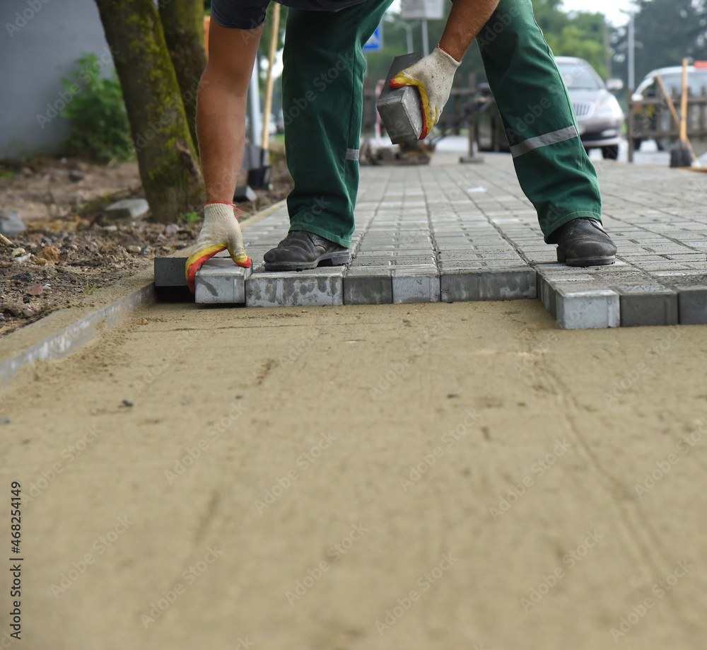 Close-up of the hands of a builder laying paving concrete tiles on sand, repair and replacement of the pavement. Close-up of the hands of a builder laying paving concrete tiles on sand, repair and replacement of the pavement.