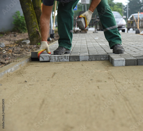 Close-up of the hands of a builder laying paving concrete tiles on sand, repair and replacement of the pavement.