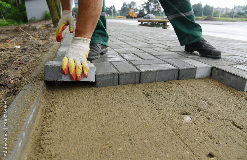 A bricklayer lays a concrete tile on the sand. Construction work on one of the road sections. A bricklayer lays a concrete tile on the sand. Construction work on one of the road sections.