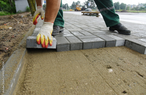 A bricklayer lays a concrete tile on the sand. Construction work on one of the road sections.