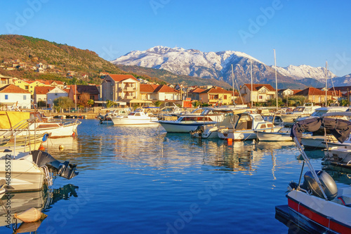 Beautiful Mediterranean landscape on sunny winter day. Fishing boats in harbor and snow-capped mountains. Montenegro, Kotor Bay. Tivat city, view of marina Kalimanj and mountains of Lovcen