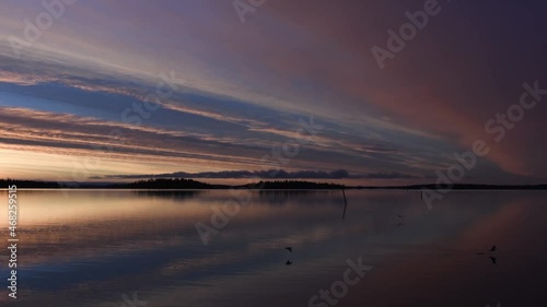 Beautiful landscape with sunrise over the lake this winter morning. Clouds and sky color reflections in the calm water. Only a few birds are awake this early morning. Footage made in Västerås, Sweden. photo