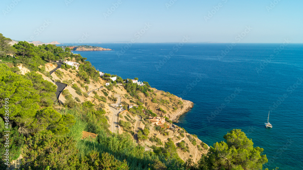 Roads and houses in front of the Mediterranean sea in Es Cubells (Ibiza, Spain). Beautiful natural landscape with houses by the sea with turquoise blue water. Views from the viewpoint of the village.