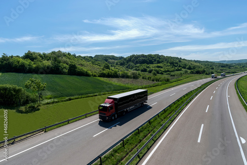 A convoy of trucks heading down the highway between meadows and dense forests. White clouds are covering the sky. Caravan or convoy of trucks in line on a country highway.   © Bojan