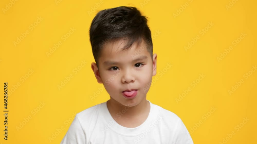 Little Japanese Boy Sticking Out Tongue Posing On Yellow Background Little Japanese Boy Sticking Out Tongue Posing On Yellow Background