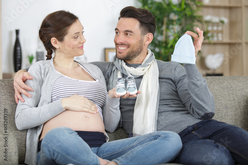 young couple with pregnant woman looking presents children clothes