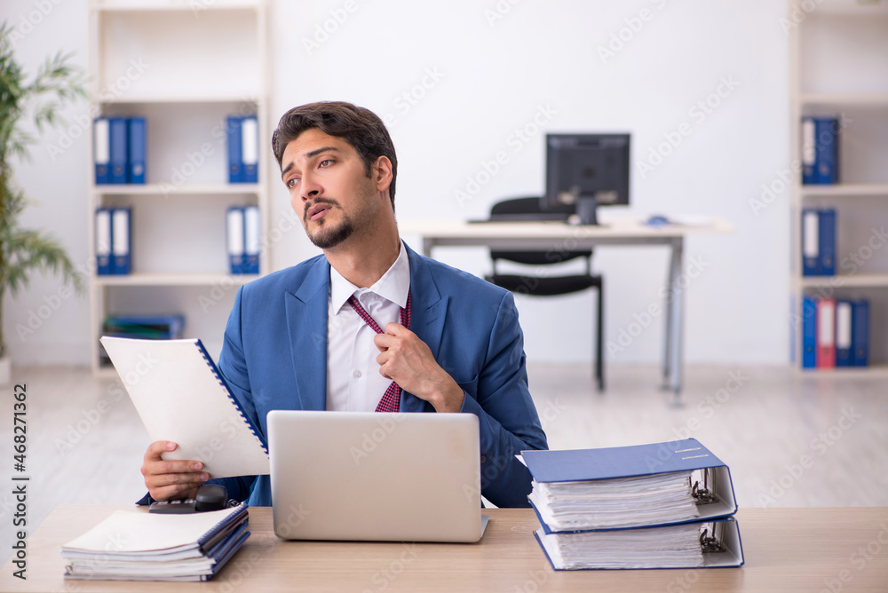 Young male employee unhappy with excessive work in the office Young male employee unhappy with excessive work in the office