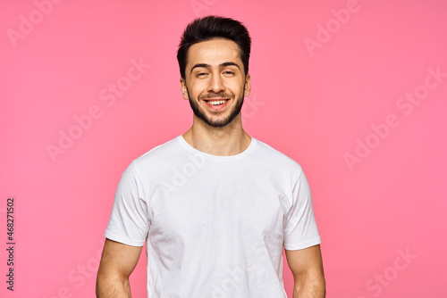 a handsome man in a white t-shirt gesturing with his hands on a pink background
