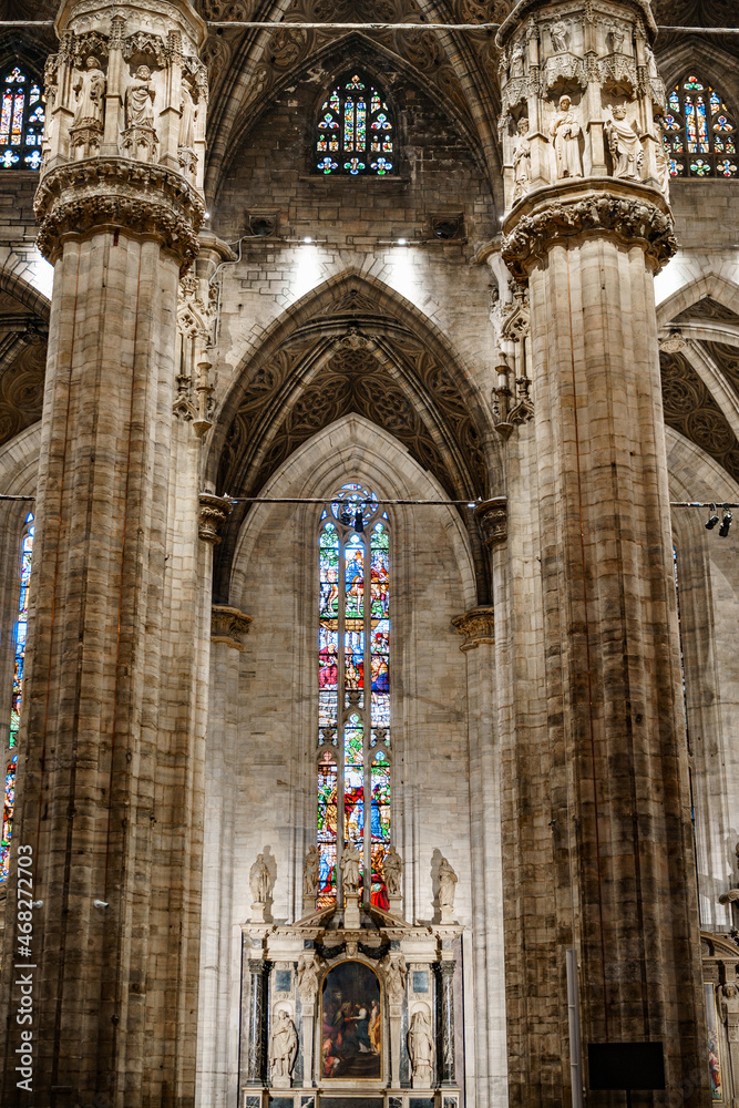 Colored stained glass windows against the huge carved marble columns of the Duomo. Italy, Milan